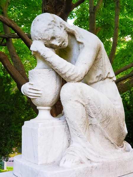 Sculpture of a sitting woman leaning on and embracing an urn.