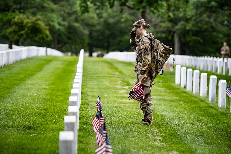 Soldier saluting in front of a row of tombstones at Arlington National Cemetery.