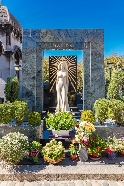 Dalida's grave in Montmartre Cemetery surrounded by flowers and plants.