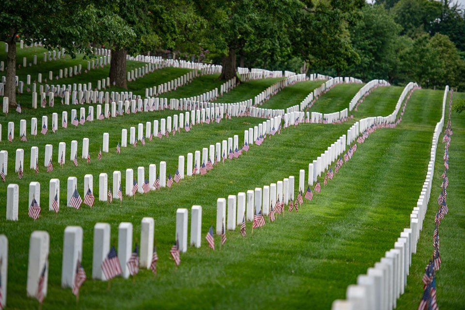 Rows of burials in Arlington National Cemetery. Small American flags are in the ground in front of each tombstone.