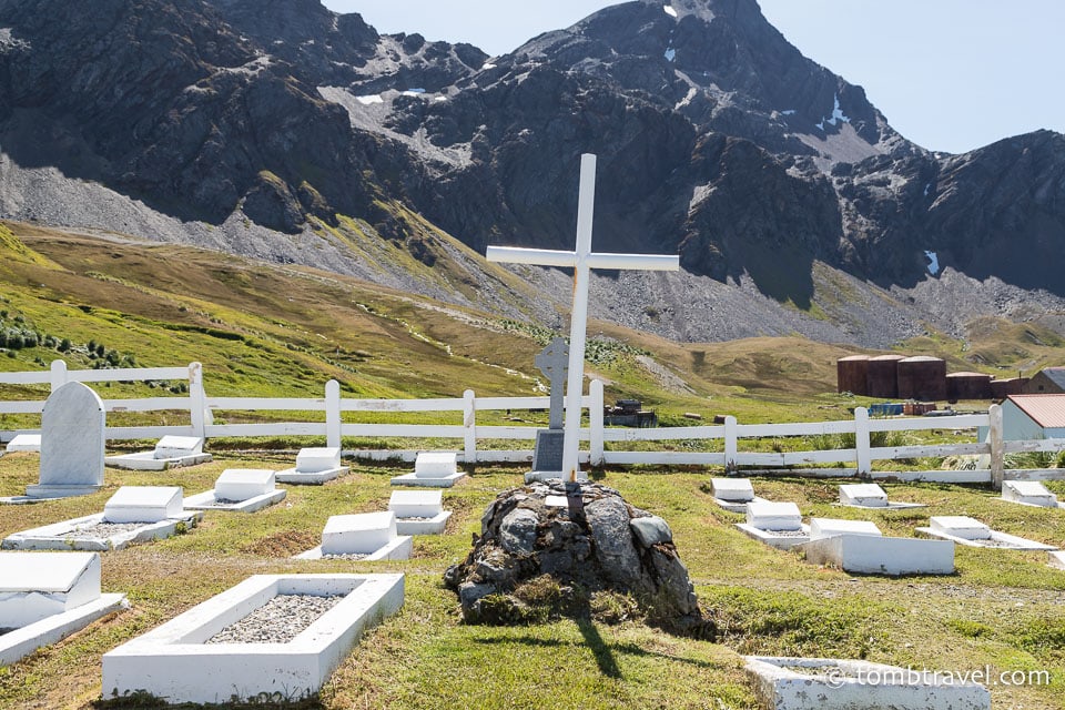 Cross and graves in the Grytviken Cemetery with a mountain in the background.