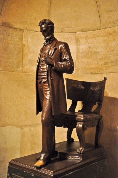Statue of Abraham Lincoln standing by a chair. It's on display in a corridor of the tomb building.