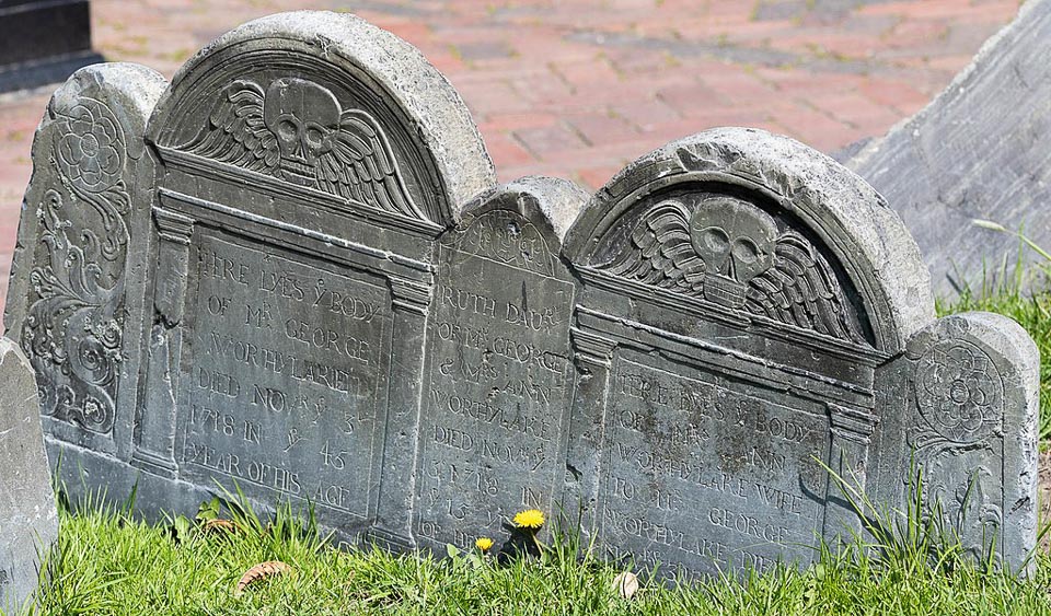 Triple headstone decorated with winged skulls.