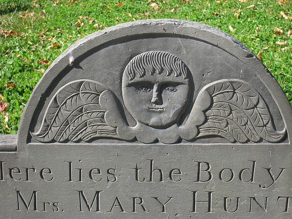 A winged cherub face carved onto a tombstone.