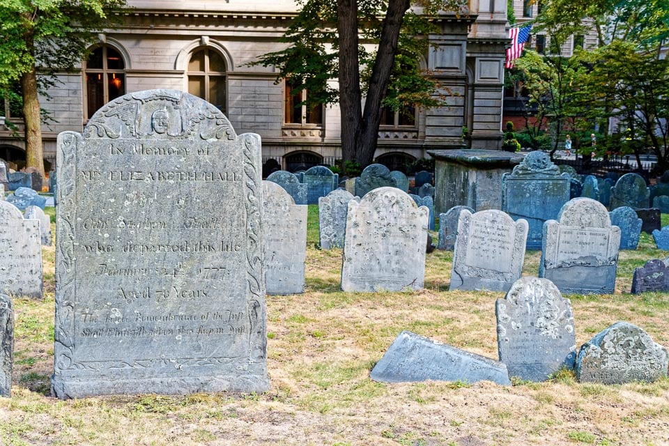 Old tombstones in Boston's Granary Burying Ground with a building in the background.