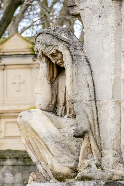 Sculpture of a mourning woman looking down with her head in her hands.