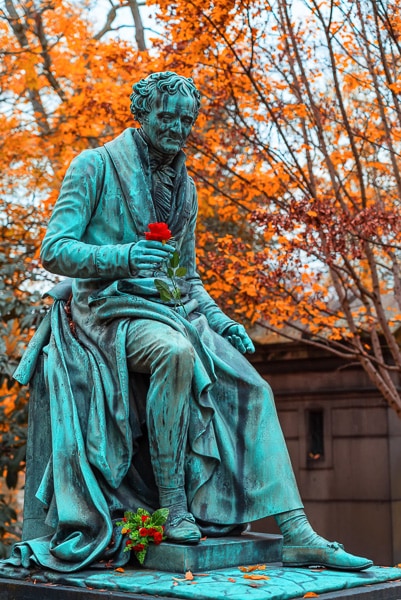 Bronze sculpture of a man sitting and holding a real rose in his hand.