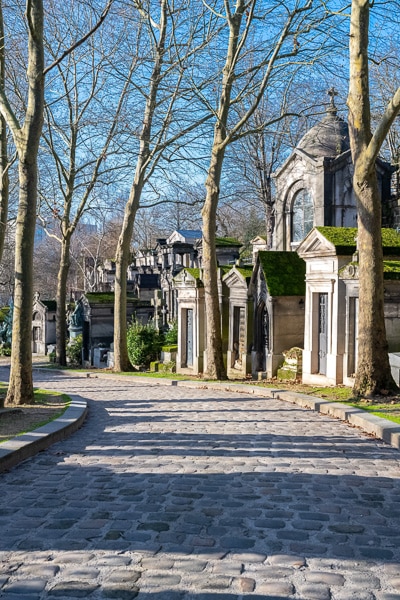 Leafless trees and mausoleums along a cobblestone path in Pere Lachaise Cemetery.