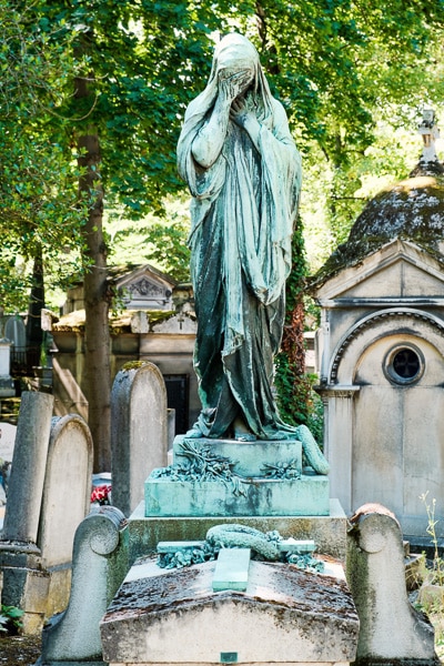 Bronze statue of a mourning woman in draped clothing covering her eyes.