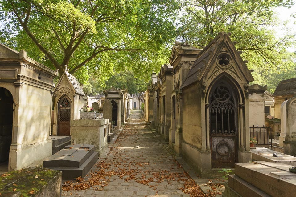 Mausoleums, tombs, and trees framing a cobblestone path in Pere Lachaise Cemetery in Paris.