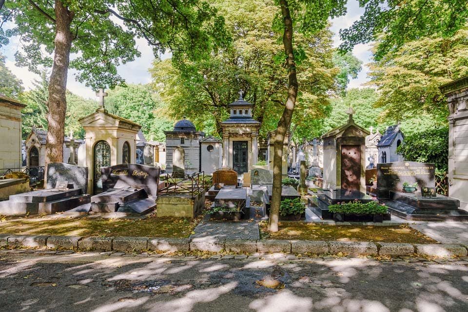 Path in front of tree-shaded tombs and graves in Montmartre Cemetery.