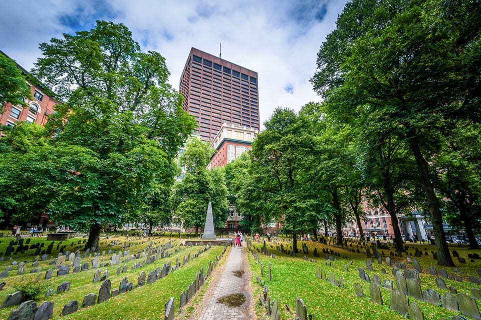 Rows of tombstones in Granary Burying Ground with an office tower in the background.