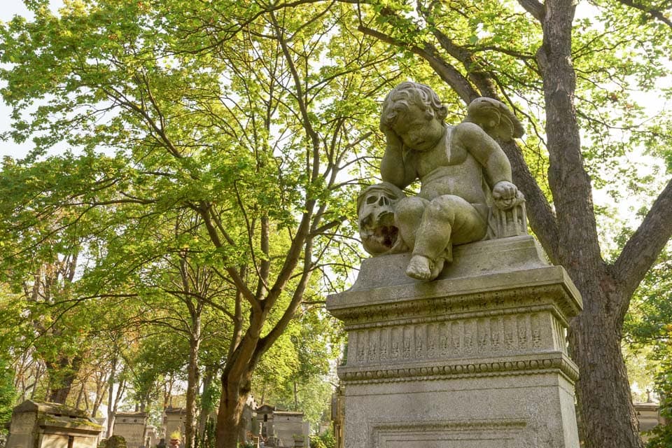 Sculpture of a winged cherub sitting in between a skull and hourglass.