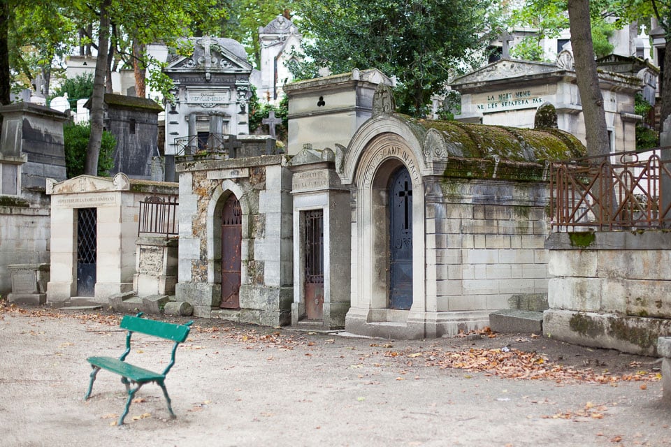 A green bench in front of some old mausoleums.