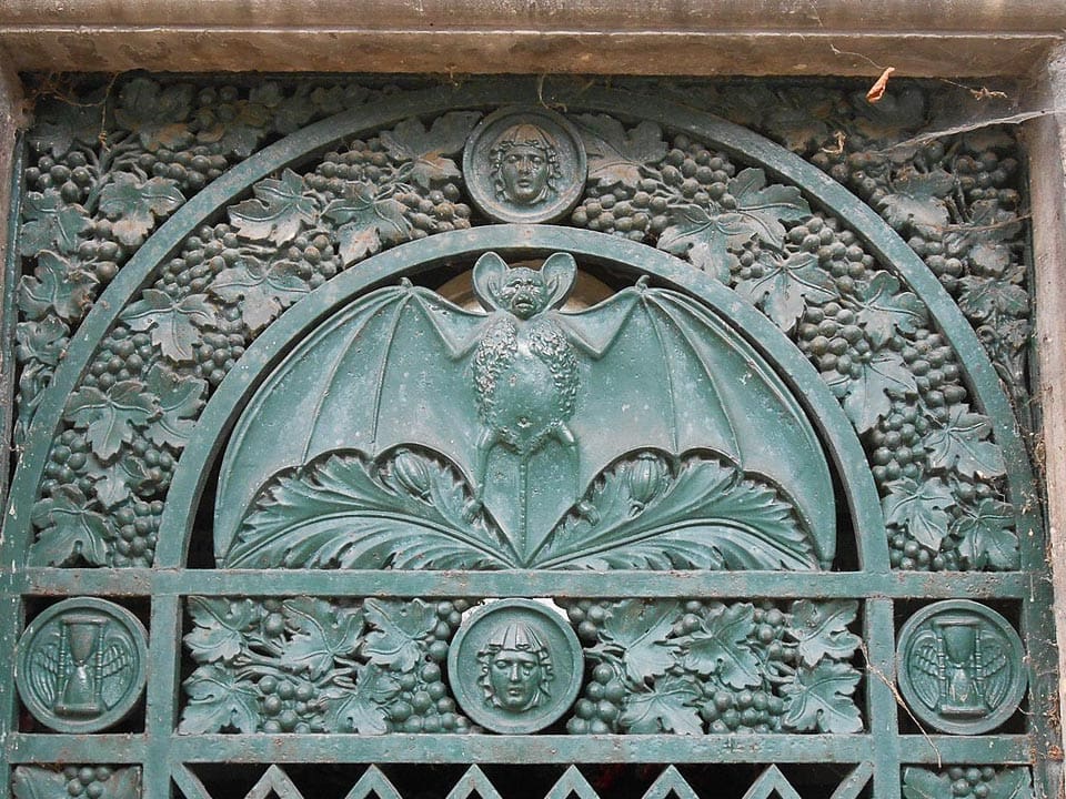 Mausoleum door decorated with a bat, grapevines, and winged hourglasses.