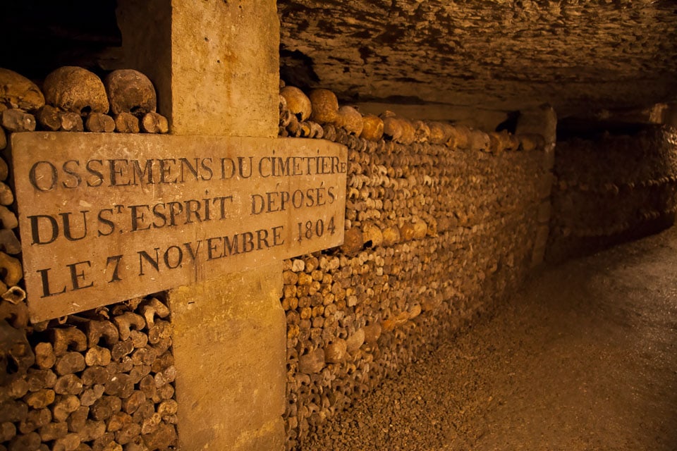 A cross beside bones lining a passageway in the Paris catacombs.