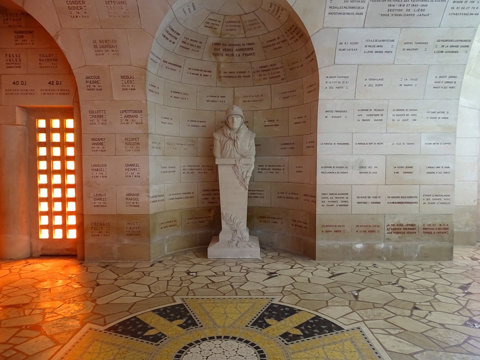 A sculpture and names on the wall inside Douaumont Ossuary.